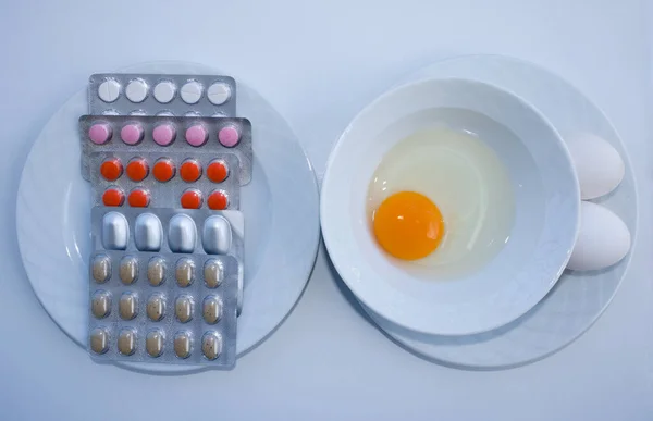Yumurta sarısı kasede. Kasede iki yumurta ve vitamin hapları. İlaç ya da sağlıklı beslenme. Hayvan kaynaklı yiyecekler ve vitaminler. B vitamini.