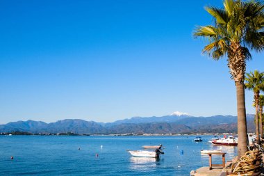 Mavi gökyüzü, mavi deniz ve kıyıda küçük balıkçı tekneleri.