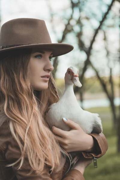 Girl in brown hat keeps white duck on her hands. Portrait of a women with a bird.