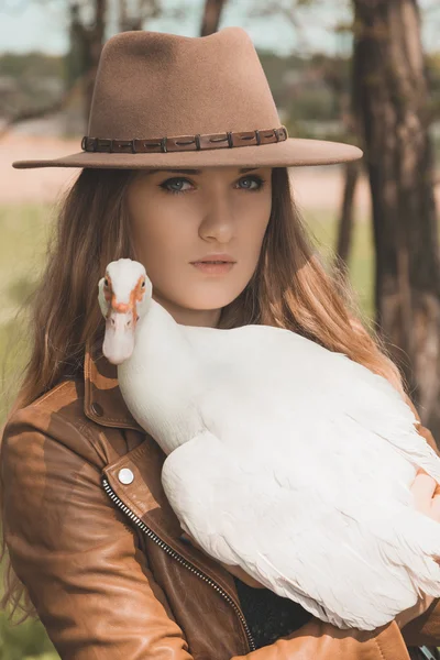 La fille au chapeau marron garde le canard blanc sur ses mains. Portrait d'une femme avec un oiseau . — Photo