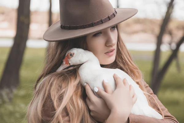 Beyaz ördek tutan bir kız portresi. Kuş doğrudan kameraya bakıyor. Ördek kafasını kızın omzuna koydu..