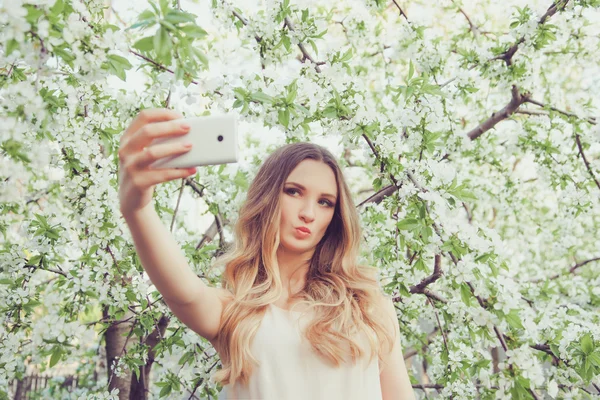 Une jeune fille pose pour la caméra sur le fond d'un arbre à fleurs. Elle prend selfie près des fleurs . — Photo