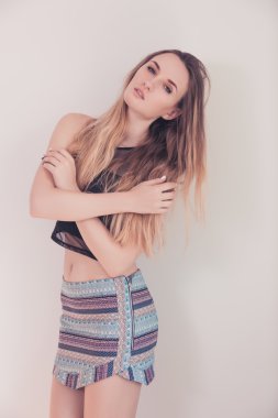 Güzel ince kız beyaz duvara poz. Kendini sarılma. O kollar göğüs üzerinde katlanmış.