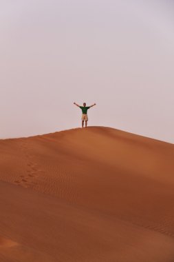 Küçük kişi çölde kum tepenin kenarında yer almaktadır. O kollarını yukarı uzanır ve başparmak-up gösterir.
