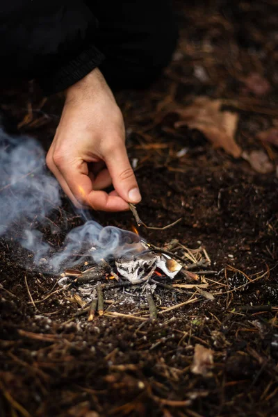 A man kindles a fire in the forest on vacation. Close-up male hand in the process of kindling a fire at a picnic in the forest