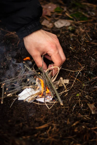A man kindles a fire in the forest on vacation. Close-up male hand in the process of kindling a fire at a picnic in the forest