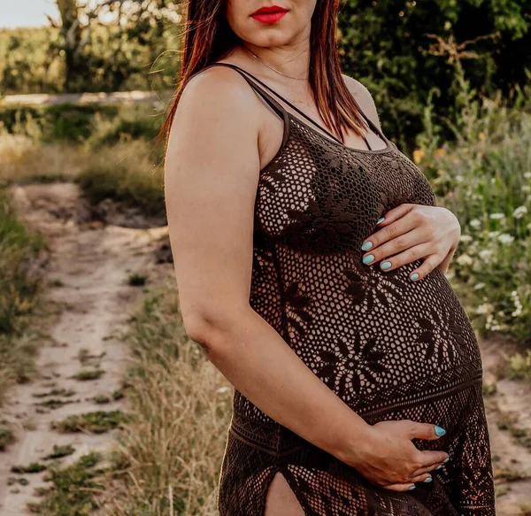 Pregnant young girl in a black mesh long dress and red lips on nature in autumn