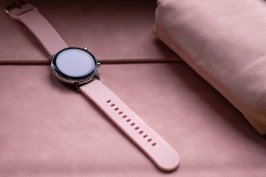 Yumuşak pembe renkli kızlar için modern aletler. Pembe kayışı olan akıllı bir saat pembe bir kozmetik çantanın yanında pembe bir dizüstü bilgisayarın üzerinde yatıyor.