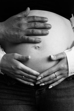 Ebeveynlerin elleri kızın hamile karnında yatar. Bebeğin gelişi için şehvetli bir fotoğraf.