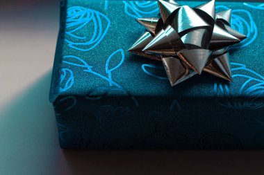 Üzerinde gümüş bir fiyonk ve güller olan mavi renkli güzel bir hediye kutusu. 