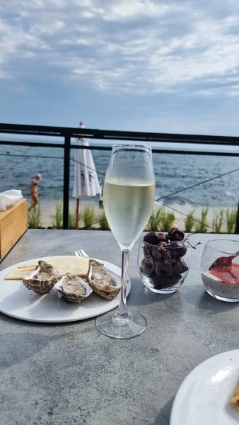 Een glas champagne met een kom mosselen en verse kersen op de tafel van het terras met uitzicht op zee — Stockfoto