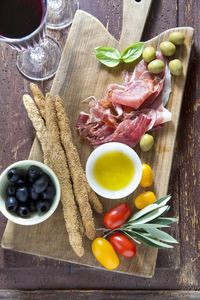 Cured meat on a wooden cutting board with red tomatoes, olives a — Stock Photo, Image