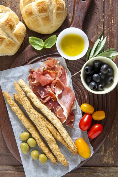 Прошутто крудо з хлібом, оливками, помідорами, хлібними паличками, олією — стокове фото
