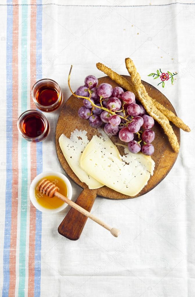 cheese snack on a wooden board with grapes, bread sticks and Ita