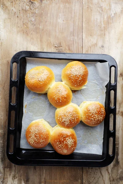 Goda bullar med Sesam på ugnen-bricka, på trä bakgrund — Stockfoto