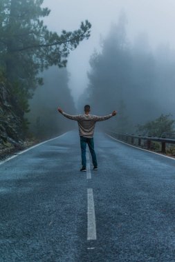 Karlı bir yolun ortasında çizgili kazak ve kot pantolon giyen bir çocuk.