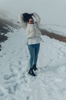 Gözlüklü ve beyaz ceketli bir kadın karlı dağlarda poz veriyor.