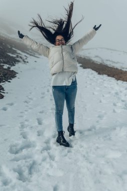 Gözlüklü ve beyaz ceketli bir kadın karlı dağlarda poz veriyor.