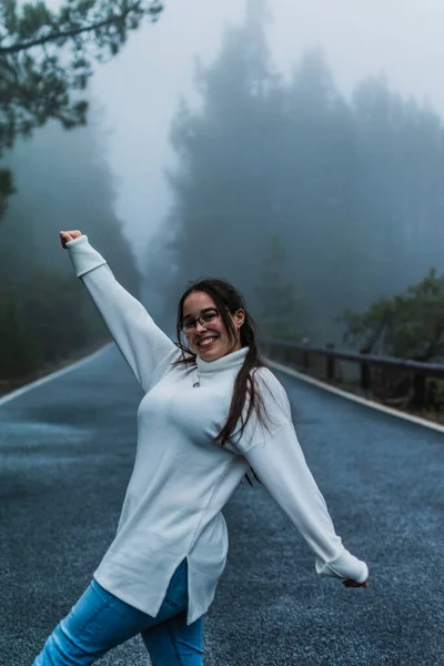 Beyaz ceketli ve gözlüklü bir kadın. Karlı bir yolun ortasında, ormanın içinde.