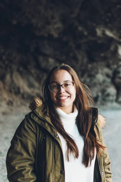 Gözlüklü, kahverengi ceketli, şapka ve kot pantolonlu bir kız.