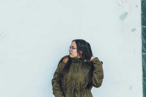 Gözlüklü, kahverengi ceketli, şapka ve kot pantolonlu bir kız.