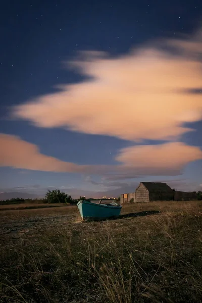 Ön planda mavi bir tekne olan bir tarlanın ortasında ahşap bir ev.