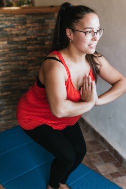 Gözlüklü ve turuncu gömlekli kız evde esneme hareketleri yapıyor.