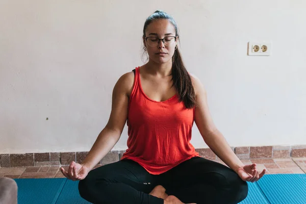 Gözlüklü ve turuncu gömlekli kız evde esneme hareketleri yapıyor.