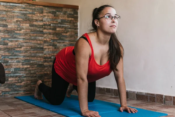 Gözlüklü ve turuncu gömlekli kız evde esneme hareketleri yapıyor.