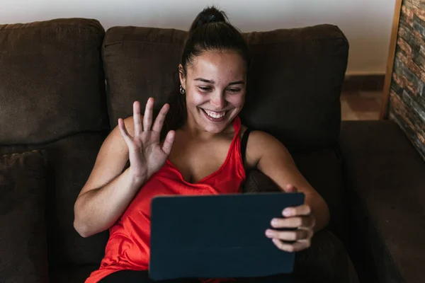 Gözlüklü ve turuncu gömlekli kız kahverengi koltukta video görüşmeleri yapıyor.