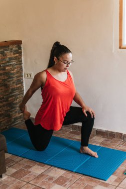 Gözlüklü ve turuncu gömlekli kız evde esneme hareketleri yapıyor.