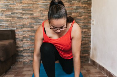 Gözlüklü ve turuncu gömlekli kız evde esneme hareketleri yapıyor.