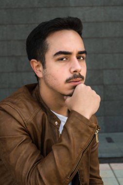 Kahverengi deri ceketli çocuk poz veriyor.