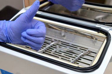 Koruyucu mavi eldivenler, arka planda bulanık dezenfekte edilmiş manikür ve pedikür aletleri olduğunu gösteriyor.