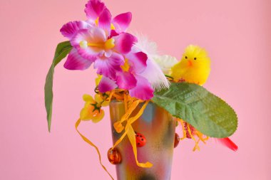Yapay orkide çiçekleriyle Paskalya kompozisyonu ve pembe arka planda seramik kapta sarı bir piliç, şenlikli ev dekorasyonu.