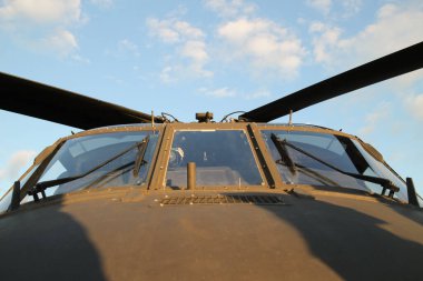 Mavi gökyüzüne karşı askeri bir helikopterin kokpit ön camının alt görüntüsü.
