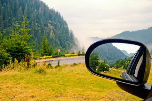 Car mirror with reflection of a mountain landscape during a trip on the Transfagarasan road in Romania.