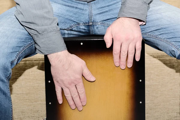 Adam cajon davulu çalıyor. Perküsyon enstrümanı çalışırken davulcunun ellerinin yakın görüntüsü.