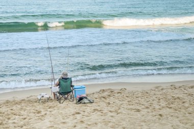 Deniz kenarındaki balıkçı. Yaşlı adam kıyıda oturur ve balıkçılıkla meşgul olur..