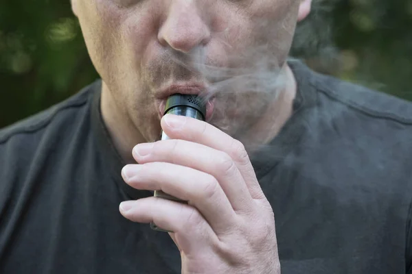 Close-up face of a man smoking an electronic cigarette. Man hold vaping device and inhales smoke. Vaping, vaporizing a liquid to inhale, popular alternative to cigarette smoking.