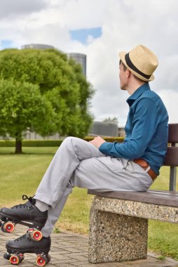 Şehrin sokaklarında paten kayarken, şehir parkındaki bankta dinlenen patenli genç adam..