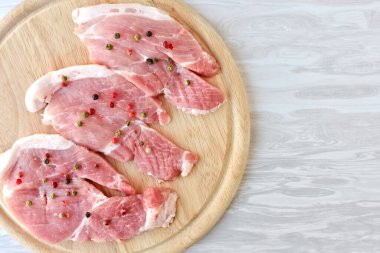 Tahta kesme tahtasında farklı biberlerle tatlandırılmış çiğ domuz pirzolası.