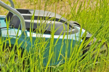 Elektrikli çim biçme makinesi ön planda odaklanmamış çimlerin arasında çim biçerken görüntüsü