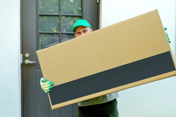 Teslimatçı evin kapısında büyük bir karton kutu tutuyor. Posta kuryesi paketi adrese teslim etti. Ulaşım ve paket teslimatında çalışıyor. Metin ve tasarım için boşluk.