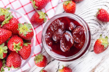 Ev yapımı lezzetli çilek reçeli ve ahşap bir masada çilek.