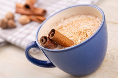 Mavi kupa salep sütlü, tarçın tozlu sıcak Türkiye içeceği ve beyaz kırsal ahşap masa üzerinde çubuklar..