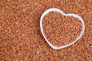 buckwheat in a white heart-shaped bowl with buckwheat textured background