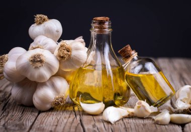 Olgun ve çiğ sarımsak ve sarımsak yağı bir bardak şişede tahta masada çuval, alternatif ilaç, organik temizleyici. 