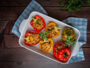 Doldurulmuş biber, pirinçle doldurulmuş yarım biber, kurutulmuş domates, otlar ve peynir mavi ahşap bir masada fırın kabında, üst manzara. (Türkçe adı; biber dolmasi)