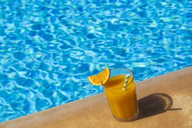 Yüzme havuzunda bir bardak taze portakal suyu, tropik yaz tatili konsepti..